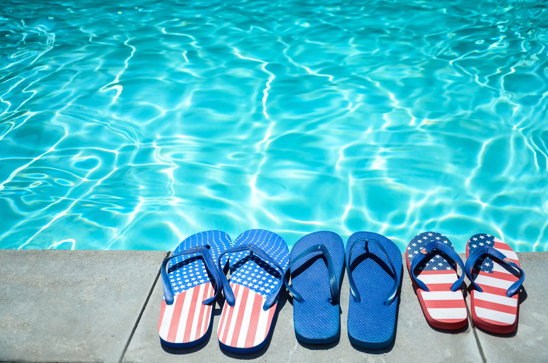 Summer background with flip flops of American flag colors and pattern near the swimming pool